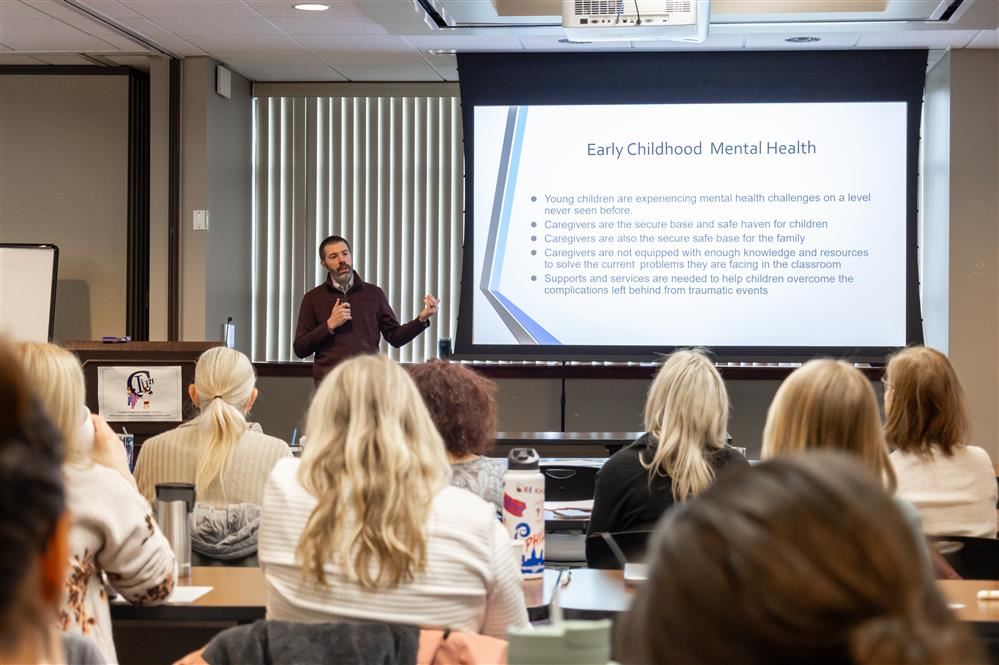  A person is speaking to a large group of people about early childhood mental health.